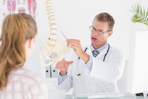 Doctor showing his patient a spine model in medical office