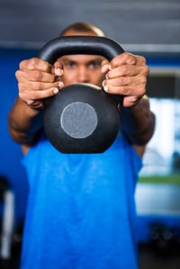 Man covering face with kettlebell while exercising in gym