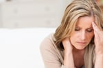 Woman suffering from stress or a headache grimacing in pain as she holds the back of her neck with her other hand to her temple, with copyspace